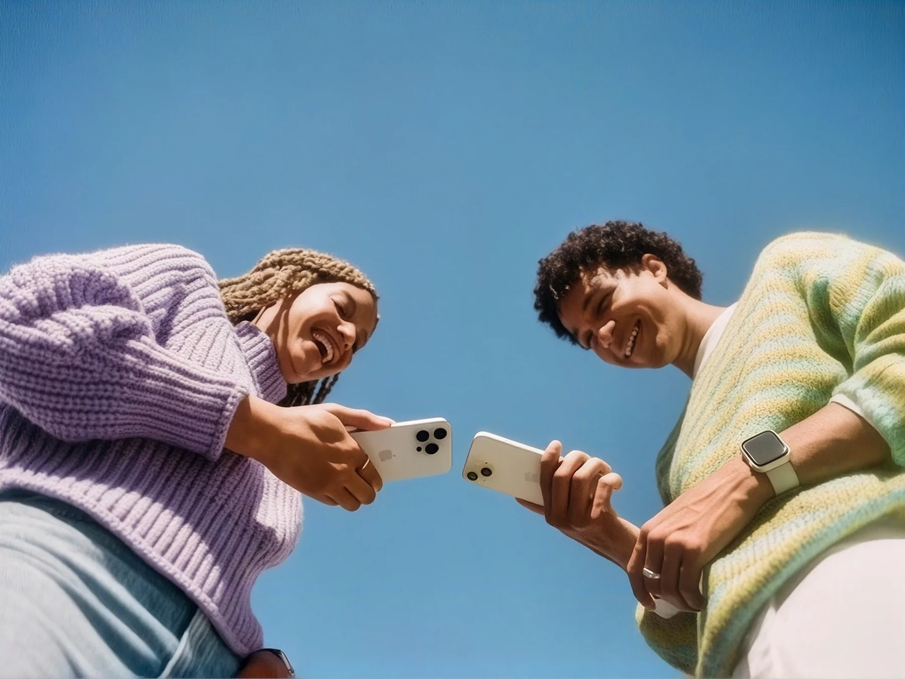 2 people standing under a blue sky, holding their phones together to send a file