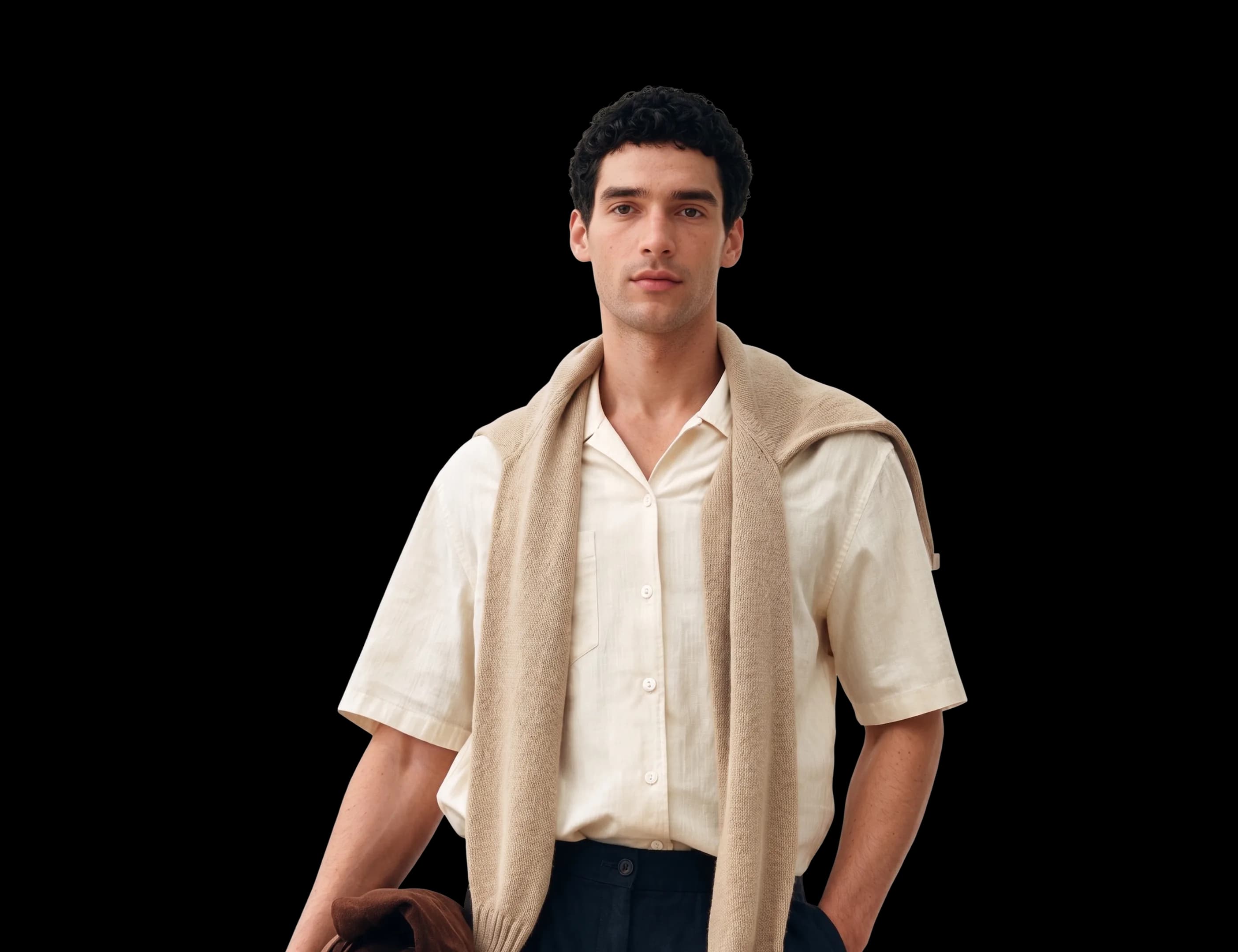 A man in a cream camp-collar shirt with a sand sweater over his shoulders and a suede jacket in his hand