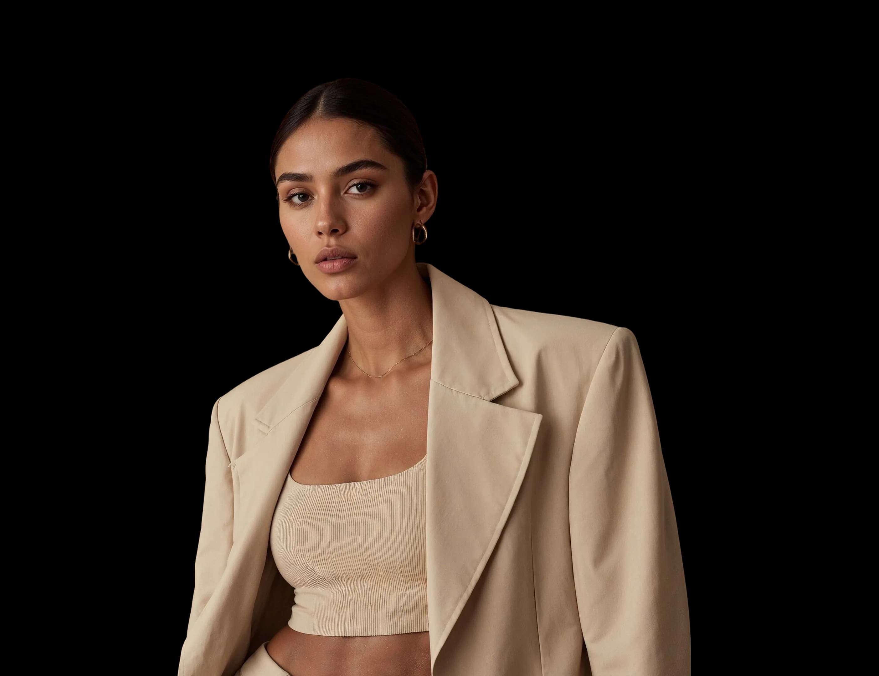 A woman in an oversized sand blazer over a ribbed crop top and pleated trousers