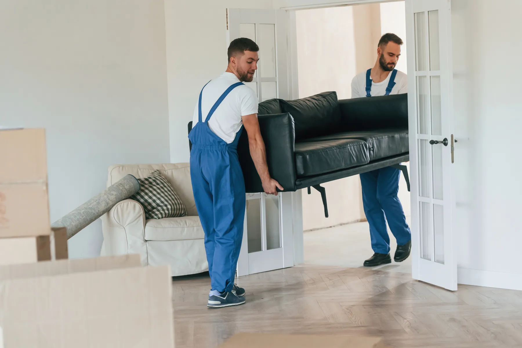 2 delivery crew members carrying a sofa into a bright living room